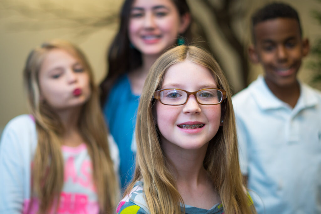 Smiling girl in glasses wearing braces with friends in the background